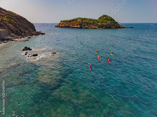 Aerial view of people kayaking in the clear blue waters of the Tyrrhenian Sea near the rocky coastline of Marina di Campo, Toscana, Italy.
