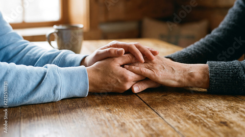 Closeup of two people holding hands on a wooden table, showing support, comfort, and emotional connection between two individuals