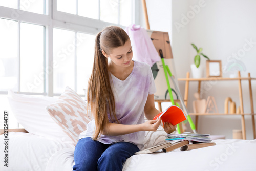 Education and self-study, young woman reading a book while sitting on a bed i...