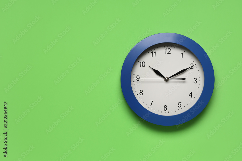 Fototapeta premium Time management and deadline pressure, blue wall clock on a green background showing ten past ten for business efficiency and punctuality concepts