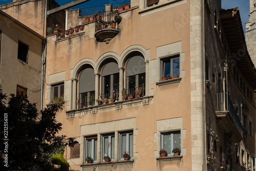 Historic Noucentisme architecture building facade in Girona, Catalonia, Spain. Beautiful residential old house with arched windows and flower pots on a sunny day.