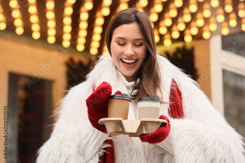 Young woman in stylish winter clothes and with cups of coffee on city street