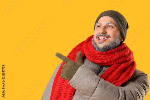 Young man in warm gloves, winter clothes and with frosted beard pointing at s...