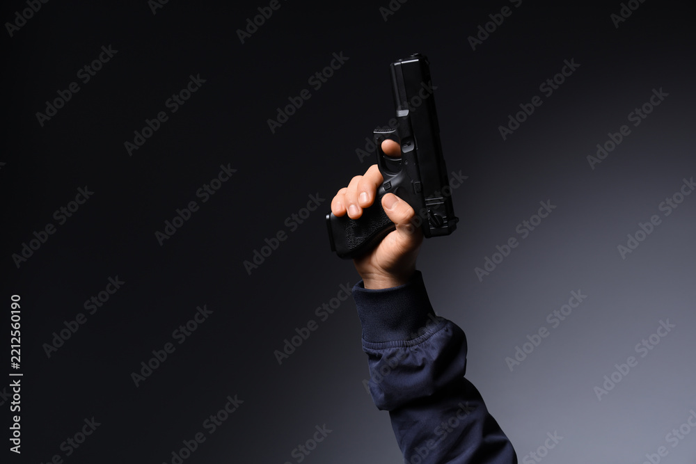 Obraz premium Gun violence and crime prevention, hand holding a black semi-automatic pistol against a dark background for law enforcement and security concepts