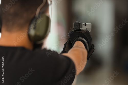 Firearm safety and target practice, man aiming handgun at indoor shooting range with protective gear and tactical gloves for marksmanship training