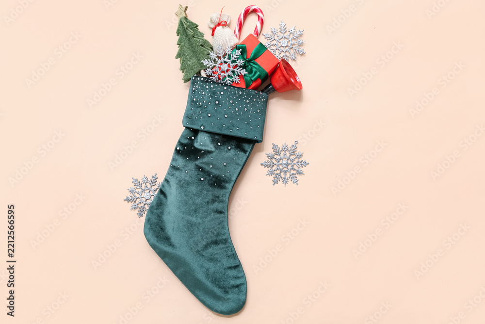 Obraz premium Christmas sock with bell, gift and decorations on beige background. Top view