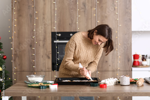 Young woman decorating gingerbread cookies in kitchen on Christmas eve