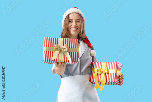 Young chambermaid with Santa hat and gifts on blue background