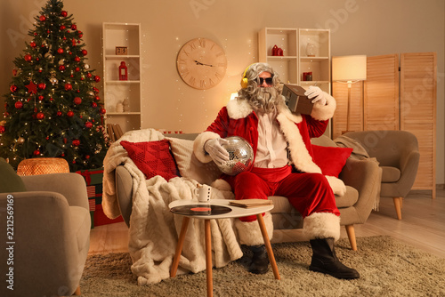Cool Santa Claus in headphones with radio receiver and disco ball sitting at ...