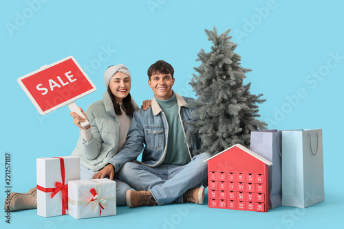 Young couple with Christmas tree, SALE sign, gift boxes and shopping bags on ...