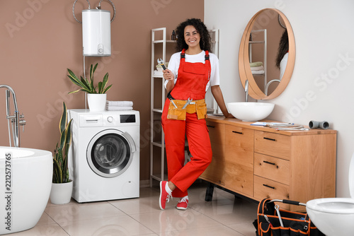 Home maintenance and plumbing services, female plumber in red overalls holdin...