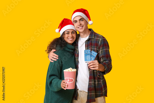Beautiful young couple in Santa hats with cinema tickets and bucket of popcor...