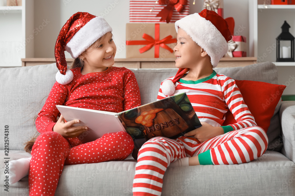 Obraz premium Cute happy little children dressed as elves reading book on Christmas at home
