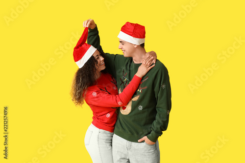 Happy young couple in Christmas sweaters on yellow background