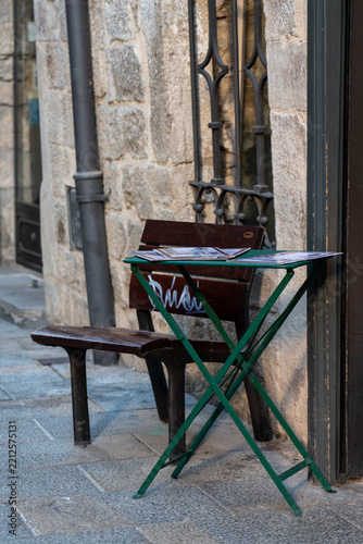 Cozy outdoor cafe table and bench on a historic cobblestone street in Girona, Spain. Traditional Mediterranean alley detail with stone walls.