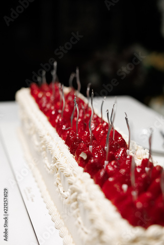 An exquisitely prepared long rectangular dessert cake, sumptuously topped with vibrant fresh red strawberries and delicate white cream frosting, creating a perfect centerpiece for elegant celebrations