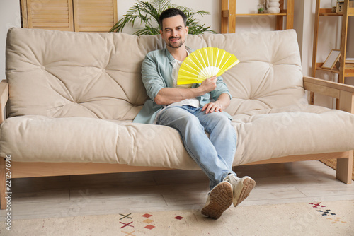 Heatwave relief and summer comfort, man cooling himself with a yellow hand fa...