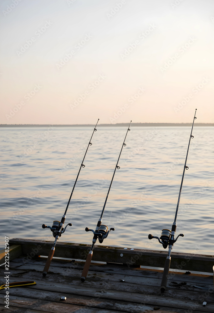 Fototapeta premium Leisure and recreation, three fishing rods set up on a wooden pier at sunset for outdoor hobby and relaxation by the calm water of a lake or river