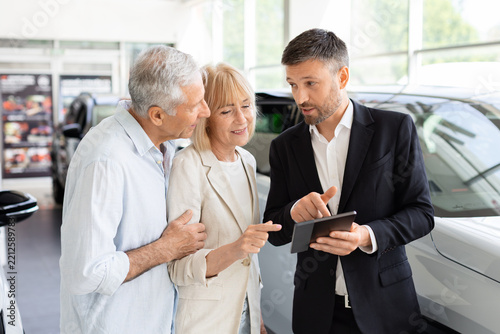 Fotografie Professional car salesperson using tablet to explain vehicle details to senior C