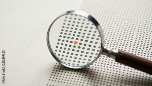 Magnifying glass highlighting single dot among grid of black dots on paper for finding anomaly, standing out and detail focused analysis