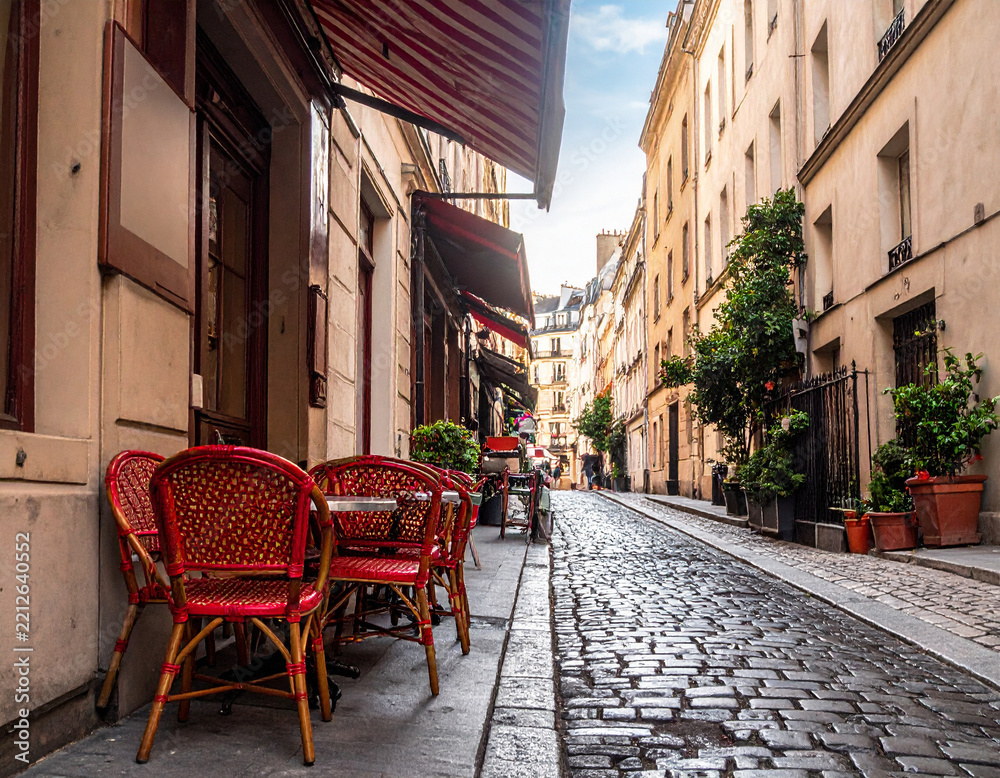 Fototapeta premium A charming, empty Parisian street with traditional red cafe chairs on a wet cobblestone alley. Nobody is present, evoking a romantic, nostalgic atmosphere perfect for travel or lifestyle themes.