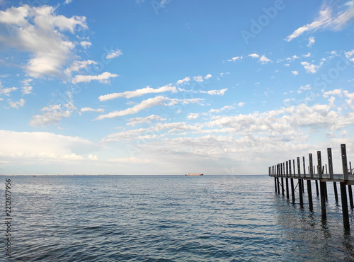 Panoramic view of calm sea surface with distant ships on the horizon under bright blue sky with fluffy white clouds, coastal landscape