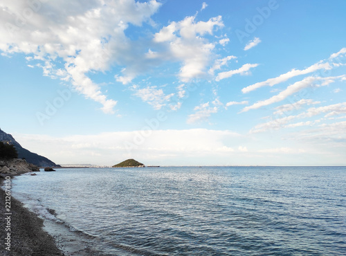 Panoramic view of calm sea surface with distant ships on the horizon under bright blue sky with fluffy white clouds, coastal landscape