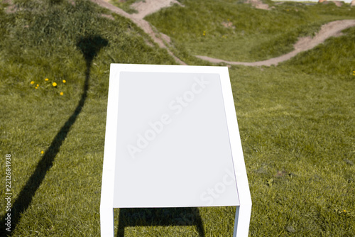 Contemporary white rectangular metal table or bench standing on a lush green lawn, with sharp shadows cast on the grass under bright sunlight. 