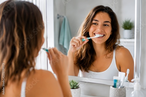 Young woman smiling, brushing teeth in bathroom mirror, practicing daily oral care for a healthy, fresh smile