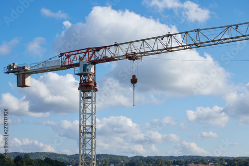 Tower crane construction equipment against blue sky and clouds. Industrial lifting machinery with a long horizontal jib and suspended hook is used for building construction and infrastructure projects