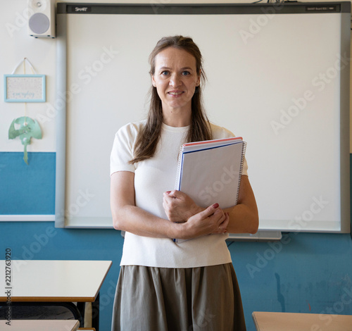 Teacher standing in a classroom holding notebooks, ready for giving lessons