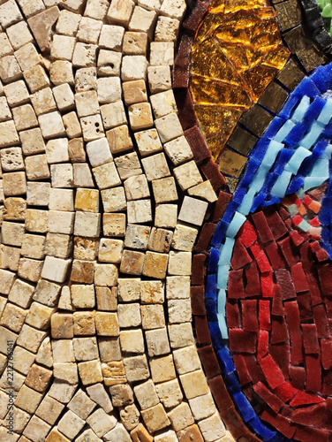 Detailed macro photograph of a multi-colored glass mosaic fragment, with small tiles arranged in flowing curved patterns. The surface is glossy and irregular, reflecting light