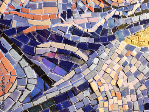 Detailed macro photograph of a multi-colored glass mosaic fragment, with small tiles arranged in flowing curved patterns. The surface is glossy and irregular, reflecting light