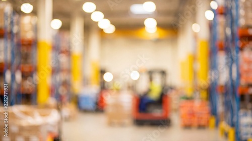 Abstract blurred background of a large modern logistics warehouse with industrial shelving units and bright bokeh lights.