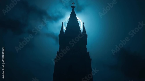 Gothic church steeple silhouette rising dramatically against glowing full moon and moody dark blue clouds motion video footage