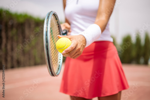 Female tennis player holding a racket and ball, ready to serve on a court.Close up