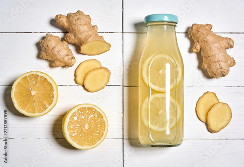 Fresh ginger root and lemon halves with homemade lemonade on white wood surface