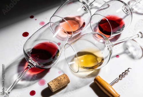 Elegant wine glasses with various wine colors lying on a bright surface with shadows