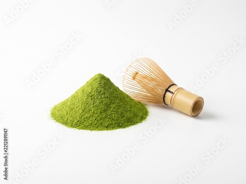 A mound of fine green matcha tea powder paired with a traditional bamboo whisk on a clean white background