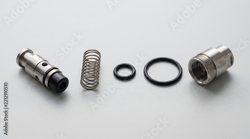 High angle detailed view of disassembled stainless steel over pressure valve internal components including spring seal and housing for espresso machine repair isolated on a clean white surface.