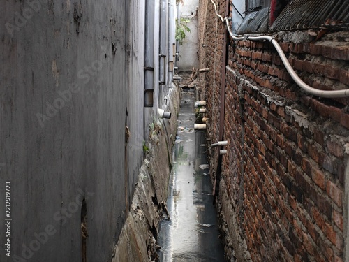 Narrow alleyway between urban buildings with a drainage ditch and brick walls