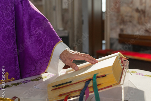 A parish priest leads a eucharistic celebration at a catholic church. The setting is focused on the priests hand on the mass book.