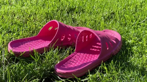 a pair of pink rubber slides rests on green grass, the open toe footwear lies side by side in a sunny outdoor setting