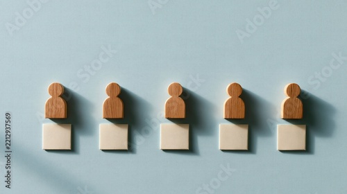 Five wooden human figures lined up on a blue background, concept of team building and recruitment.