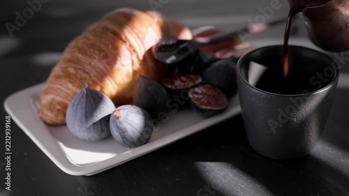 Early breakfast setting, Turkish coffee in a cezve and a croissant with figs drizzled with honey on a dark table in the morning sunlight, close-up and real-time footage