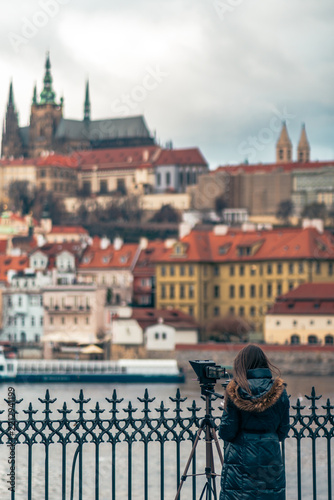 A person in a dark blue winter coat with a fur-lined hood, Prague, under an overcast sky. Selective focus