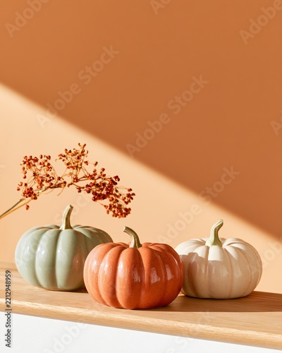 Three ceramic pumpkins in earthy colors sit on a wooden surface with flowers