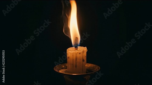 A burning candle with a bright flame against a dark background