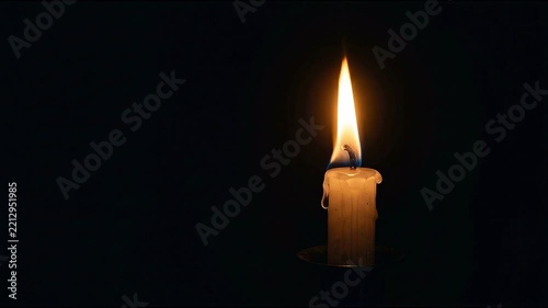 A burning candle with a bright flame against a dark background