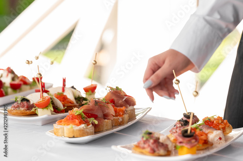 Catering service at an event. A waiter serving a variety of delicious appetizers, canapes, and finger foods on white plates at a banquet table.